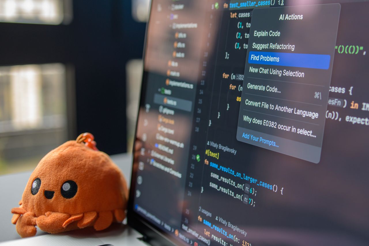 Home A laptop screen showing a code editor with a cute orange crab plush toy beside it.